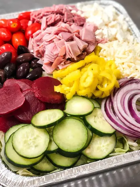 A catering tray with cucumbers, beets, banana peppers, onion, ham and cheese