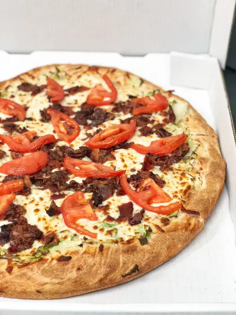 A whole hand-panned pizza loaded with bacon and tomato